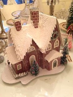 a small house with snow on the roof and trees around it, sitting on a table