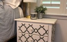 a white dresser with black and white designs on it next to a bed in a bedroom