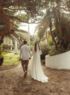 the bride and groom are walking through the palm trees in their wedding day attire, holding hands