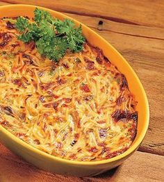 a yellow casserole dish with cheese and parsley on top sits on a wooden table