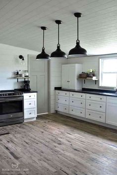 a kitchen with white cabinets and black counter tops, three pendant lights over the stove