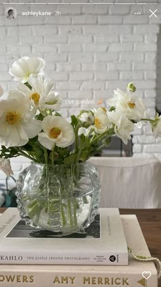 white flowers are in a glass vase on top of two books