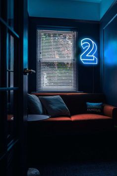 a living room with a couch, window and two neon signs on the wall above it