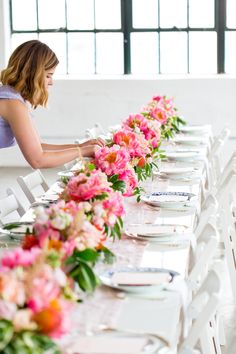 a long table with white chairs and pink flowers on the tables along side each other