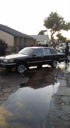 a black car parked on the side of a road next to a puddle covered sidewalk