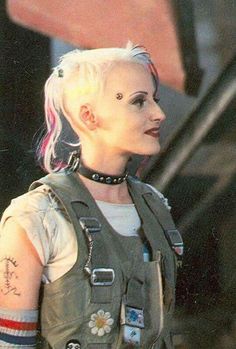 a woman with pink hair and piercings on her head is wearing a leather vest