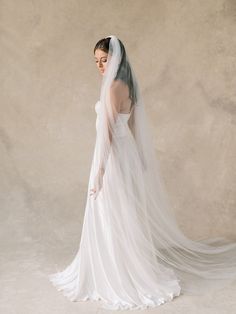 a woman in a wedding dress with a veil on her head is looking back at the camera