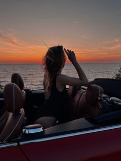 a woman sitting in the driver's seat of a convertible car looking out at the ocean