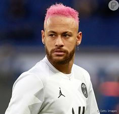 a male soccer player with pink hair and piercings on his ears is looking at the camera