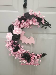 a pink and black wreath with flowers on the front door is decorated with a bat