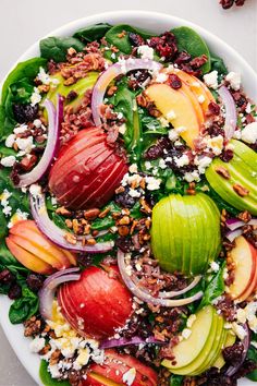 a salad with spinach, apples, onions and feta cheese is shown in a white bowl