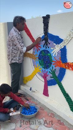 two men working on an art project made out of legos and plastic bottles in front of a wall