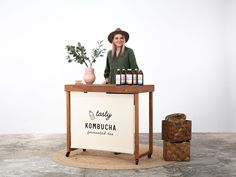 a woman standing behind a counter with bottles on it and a plant in the background