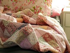 an unmade bed with pink and green quilts