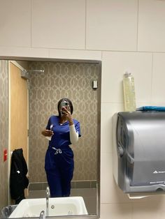 a woman taking a selfie in a bathroom mirror with a hand towel dispenser