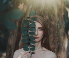 a woman is standing in front of a tree with green leaves on it's branches