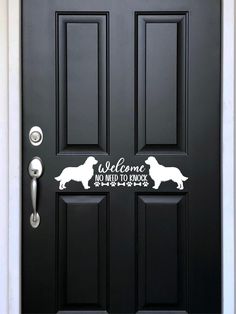 a black door with a white sign that says welcome and two dogs are on it