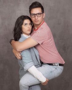 a man and woman hugging each other in front of a gray background with glasses on