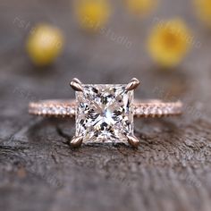 an engagement ring with a princess cut diamond in the center on top of a piece of wood