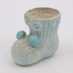 a small ceramic boot with two balls on the inside of it's side, against a white background