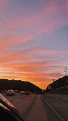 cars driving down the road at sunset with mountains in the backgrouund and clouds in the sky