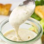 a spoon full of mayonnaise being held over a jar with broccoli in the background