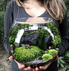 a woman holding a bowl filled with moss and rocks in the shape of an animal