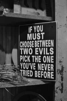 black and white photograph of a sign that says if you must choose between two evils pick the one you've never tried before