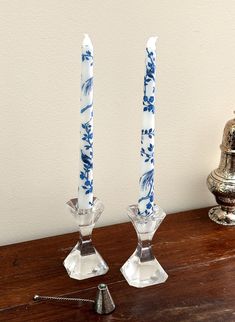 two glass candlesticks sitting on top of a wooden table next to a candle holder