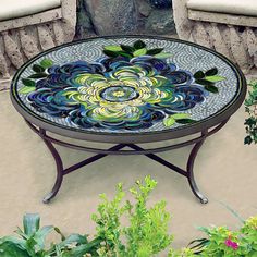 a glass table sitting on top of a patio next to some plants and flowers in front of a stone wall