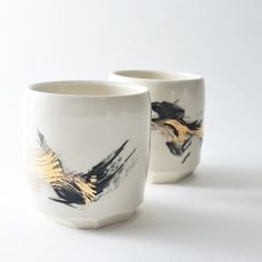 two white cups with black and gold designs on the sides, one has a yellow bird