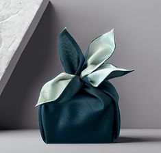 a teal satin bag with a bow on the front, sitting against a gray background