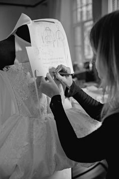 a woman in black and white writing on a piece of paper next to a wedding dress