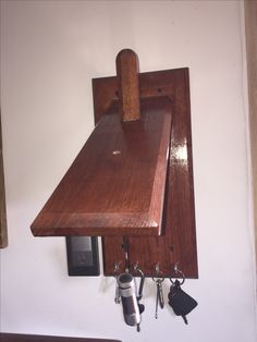 a wall mounted wooden shelf with hooks and keys hanging from it's side, next to a phone