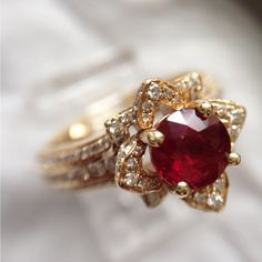 a close up of a ring with a red stone in the middle and white diamonds around it