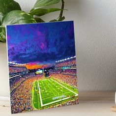 a painting of a football stadium at night art boarder on a table next to a potted plant