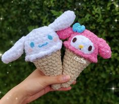 two handmade ice cream cones with hello kitty and owl faces on them are held in front of a hedge