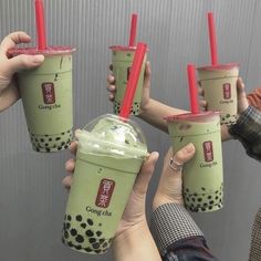 four people holding up green drinks with red straws