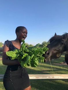 a woman standing next to a horse and eating lettuce