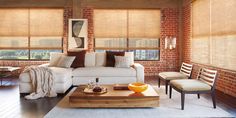 a living room with brick walls and wooden floors, white couches and chairs in front of the windows