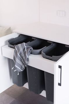 two black trash cans sitting on top of a white shelf next to a towel and shoes