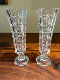 two clear glass vases sitting on top of a wooden table next to each other