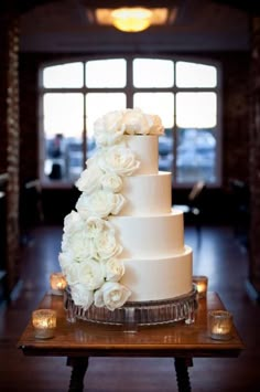 a wedding cake with white flowers is on a wooden table in front of a window