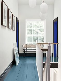 a hallway with blue flooring and white walls, framed pictures on the wall next to it