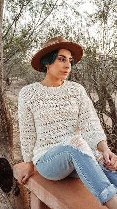 a woman with green hair sitting on a bench wearing a brown hat and blue jeans