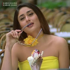 a woman in a yellow dress is eating an ice cream sundae with a spoon