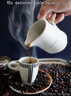 coffee being poured into a cup from a saucer on top of roasted coffee beans