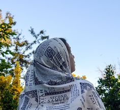 a woman wearing a shawl looking up at the sky with trees in the background