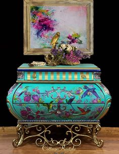 an ornate blue chest with flowers on it and a painting above the top that is framed