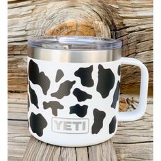 a white and black cow print yeti coffee mug sitting on top of a wooden table